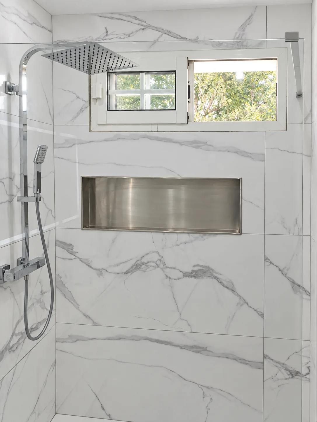 Douche avec paroi vitrée, colonne chromée, niche murale et fenêtre